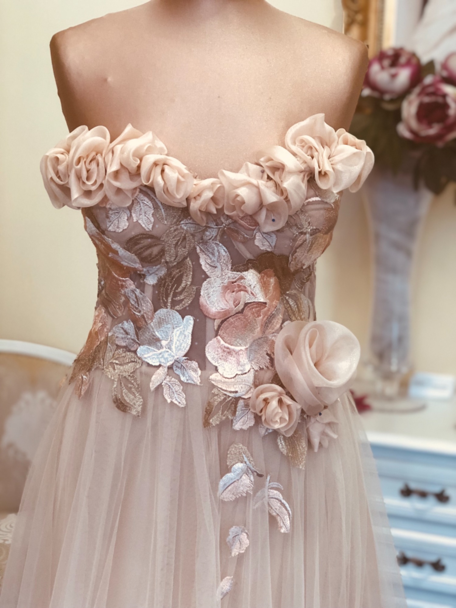 Suknia balowa w odcieniach pudrowego różu z kwiatowymi aplikacjami na manekinie, widoczne detale haftu i tiulowy dół.
