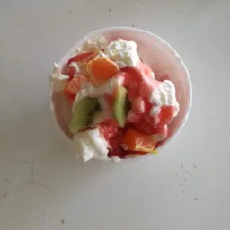 Deser lodowy z bitą śmietaną, sosem truskawkowym, kiwi i mandarynkami w plastikowym kubku, widok z góry.