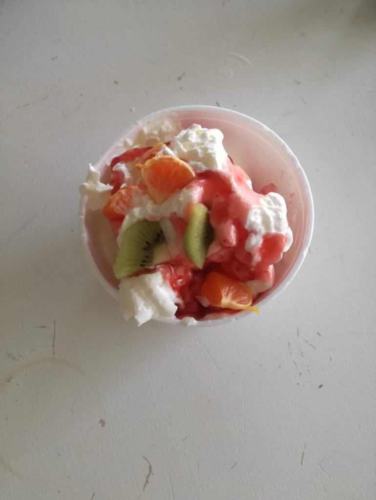 Deser lodowy z bitą śmietaną, sosem truskawkowym, kiwi i mandarynkami w plastikowym kubku, widok z góry.