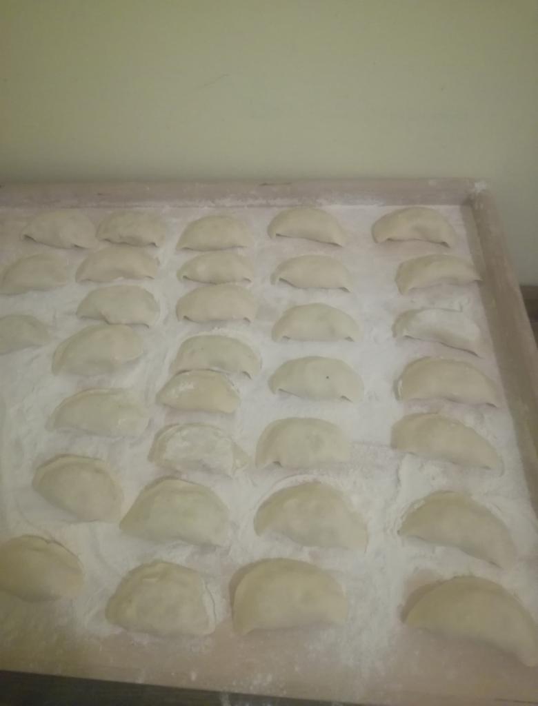 Ręcznie lepione pierogi ułożone w rzędach na drewnianej tacy posypanej mąką.