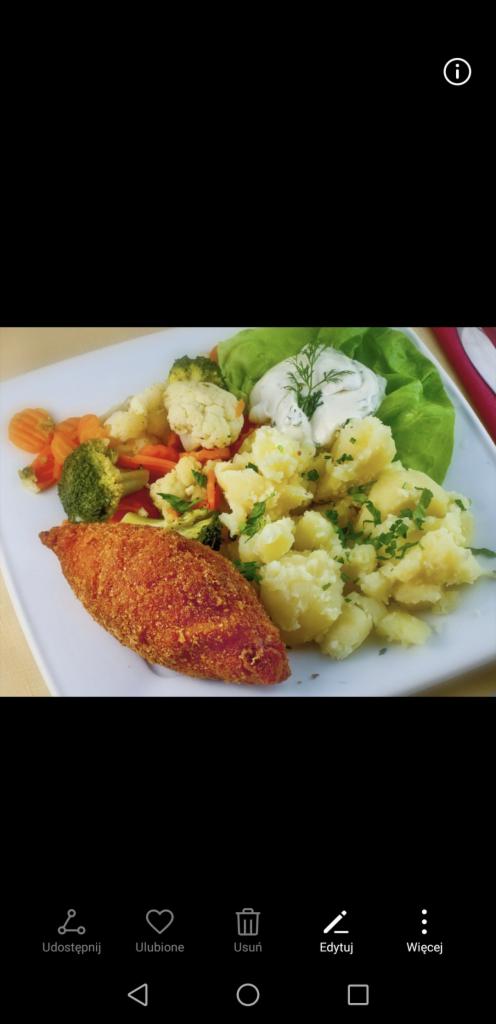 Kotlet mielony w panierce z ziemniakami posypanymi koperkiem, gotowaną marchewką i brokułami, oraz sałatą z sosem na białym kwadratowym talerzu.