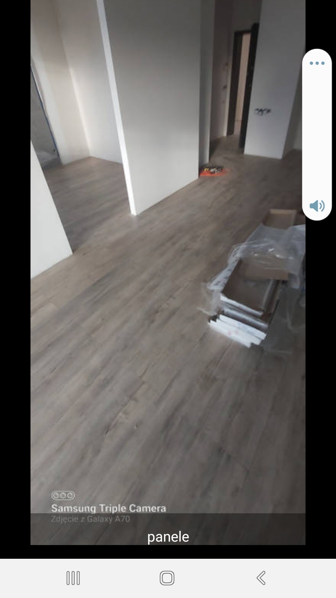 Ułożone szare panele podłogowe w nowym mieszkaniu, widoczne paczki paneli w folii i kartonach, białe ściany i framugi drzwi w tle.