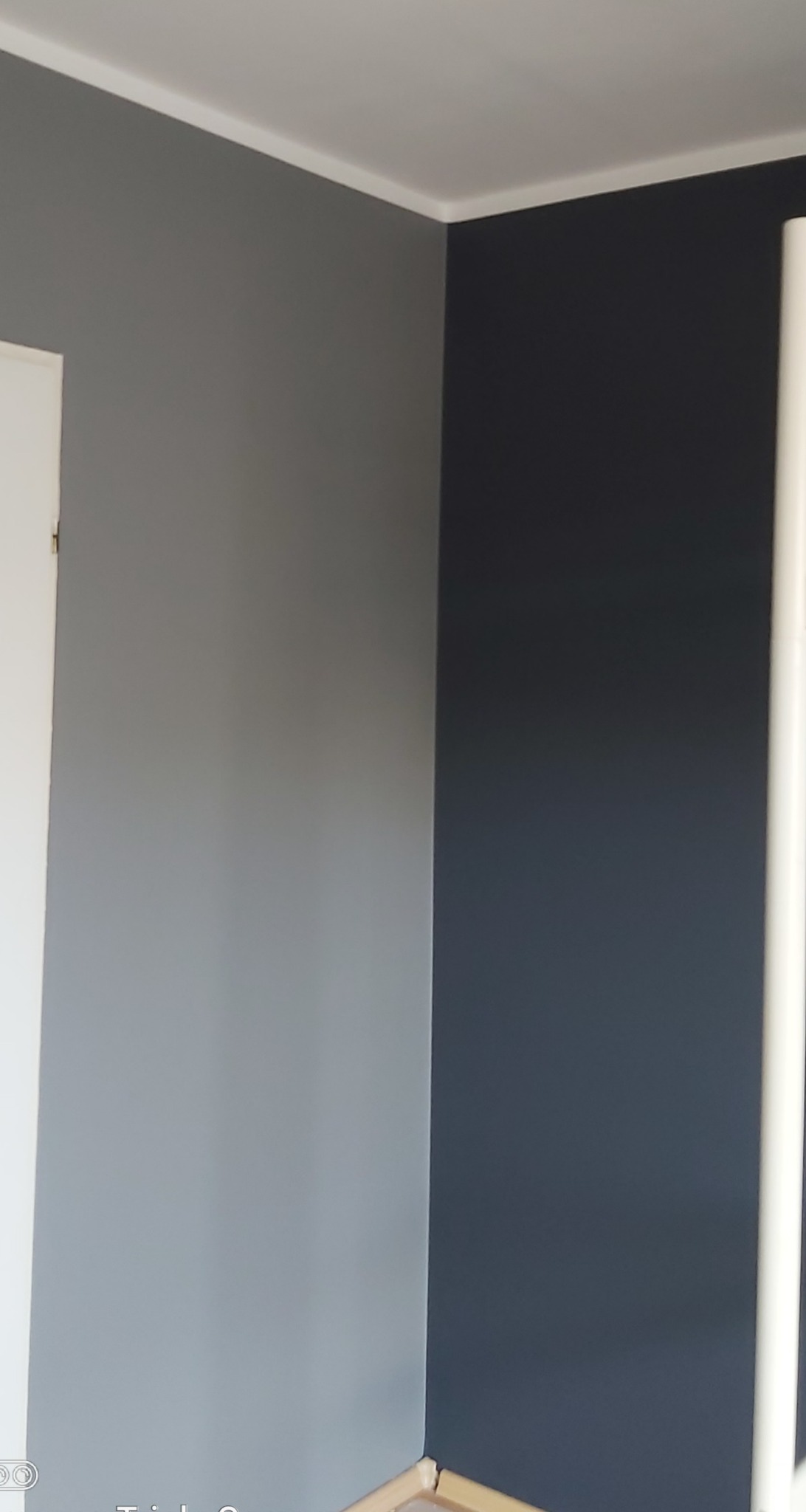 Pomieszczenie po malowaniu ścian na dwa kolory: szary i granatowy, z widoczną białą listwą przypodłogową i narożnikiem.