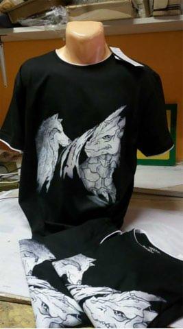 Czarna koszulka z nadrukiem przedstawiającym wilka i smoka, zaprezentowana na manekinie, obok leży kolejna koszulka z podobnym motywem.