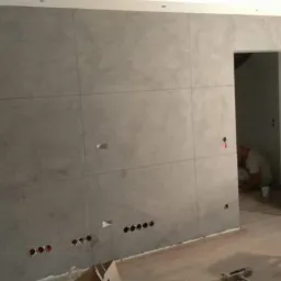 Ściana z efektem betonu architektonicznego w Olkuszu, podzielona na kwadratowe panele, widoczne gniazdka elektryczne i narzędzia pracy na podłodze.