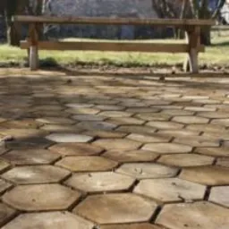 Ułożona nawierzchnia z heksagonalnych płyt betonowych w odcieniach beżu i brązu, z widoczną drewnianą ławką w tle.