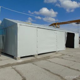 Olplan- plandeki, produkcja i naprawa - Duży, szary namiot magazynowy z plandeki na betonowej nawierzchni, z widocznym żurawiem w tle i błękitnym niebem.