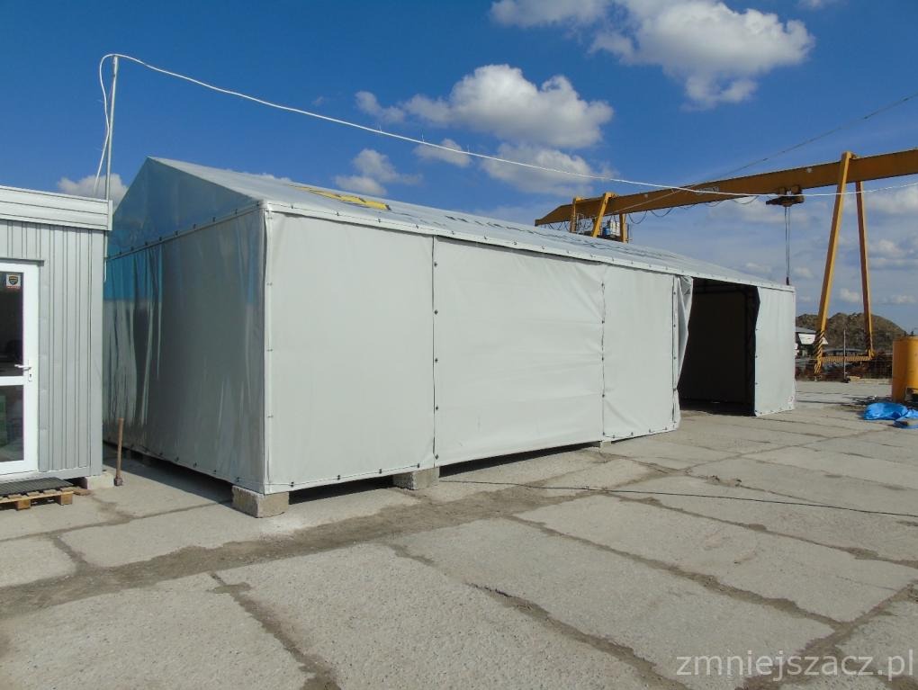 Duży, szary namiot magazynowy z plandeki na betonowej nawierzchni, z widocznym żurawiem w tle i błękitnym niebem.