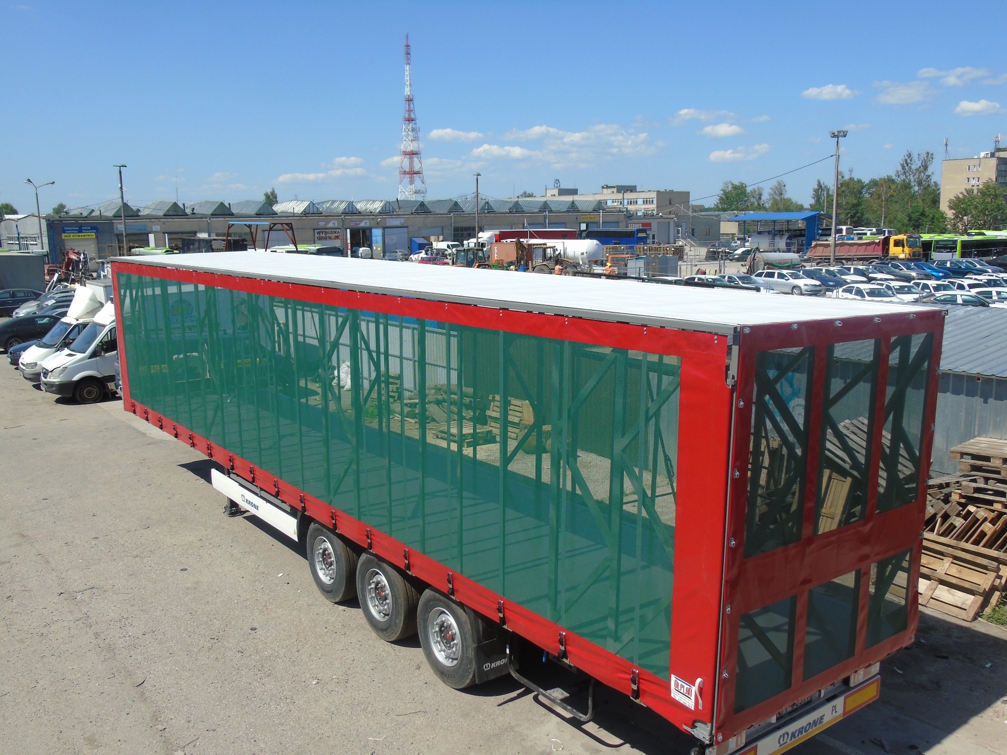 Czerwona naczepa ciężarówki z zielonym pokrowcem siatkowym, widok z góry na placu postojowym.