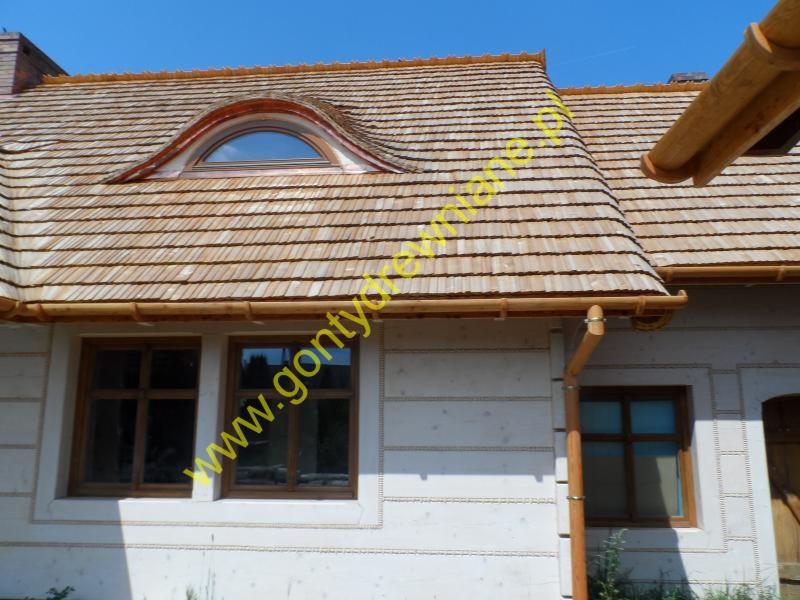 Dom z dachem pokrytym drewnianymi gontami, widoczne okno w kształcie półksiężyca na dachu i drewniana rynna.