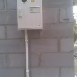 Zamontowana skrzynka elektryczna z białym przewodem na szarej ścianie z bloczków betonowych.