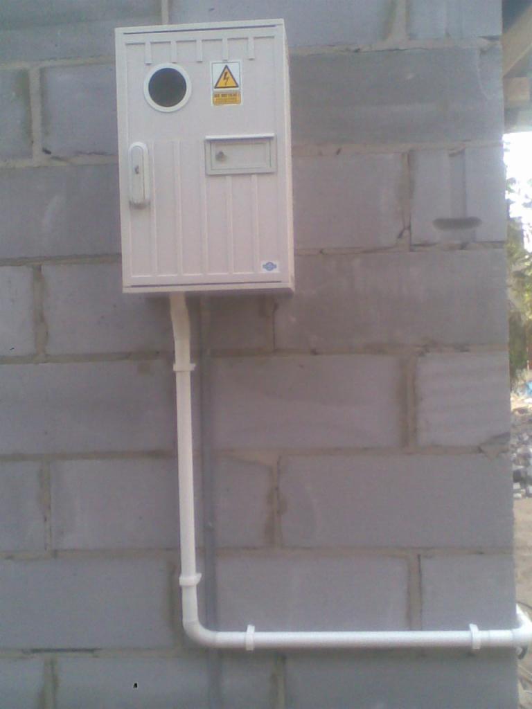 Zamontowana skrzynka elektryczna z białym przewodem na szarej ścianie z bloczków betonowych.