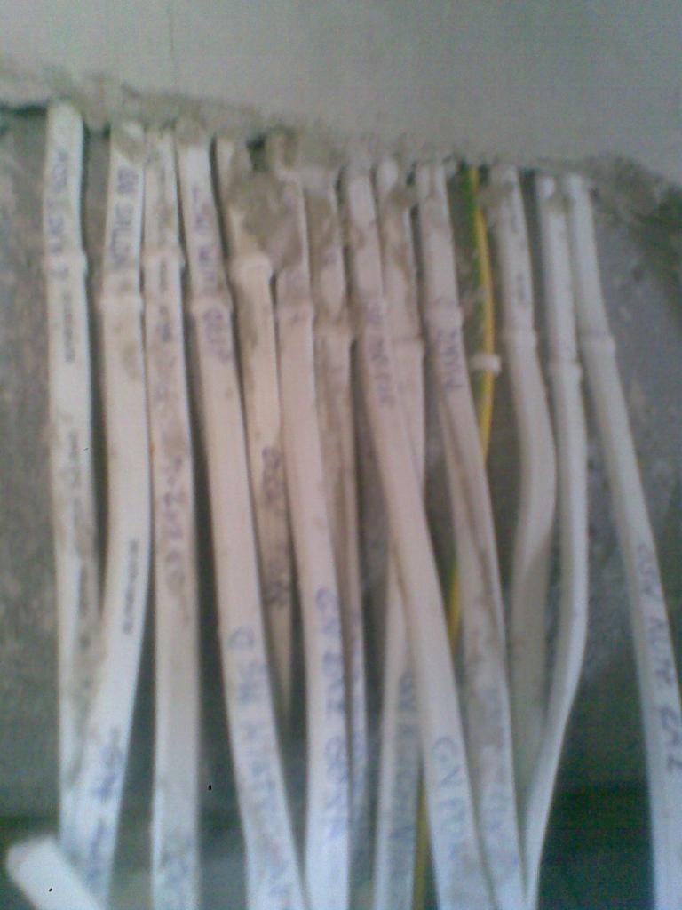 Świeżo zamontowane, białe rurki instalacyjne elektryczne, częściowo pokryte zaprawą, wystające ze ściany; widoczna jedna żółta rurka.