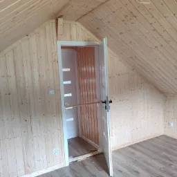 Wnętrze poddasza wykończonego boazerią w Głogowie Małopolskim, widoczne otwarte drzwi do garderoby z drewnianą półką i listwami przypodłogowymi.