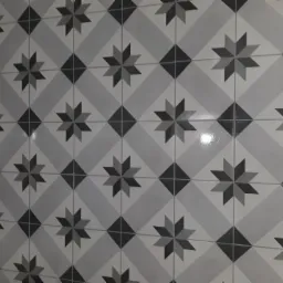 Świeżo ułożone, błyszczące, szaro-białe płytki podłogowe z motywem gwiazd i rombów, ułożone pod kątem, z widocznym fragmentem nieukończonej ściany po prawej stronie.