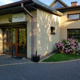 Elewacja budynku biura rachunkowego Meritex z logo nad wejściem, ozdobiona hortensjami w drewnianej donicy i kotem w ogrodzie.