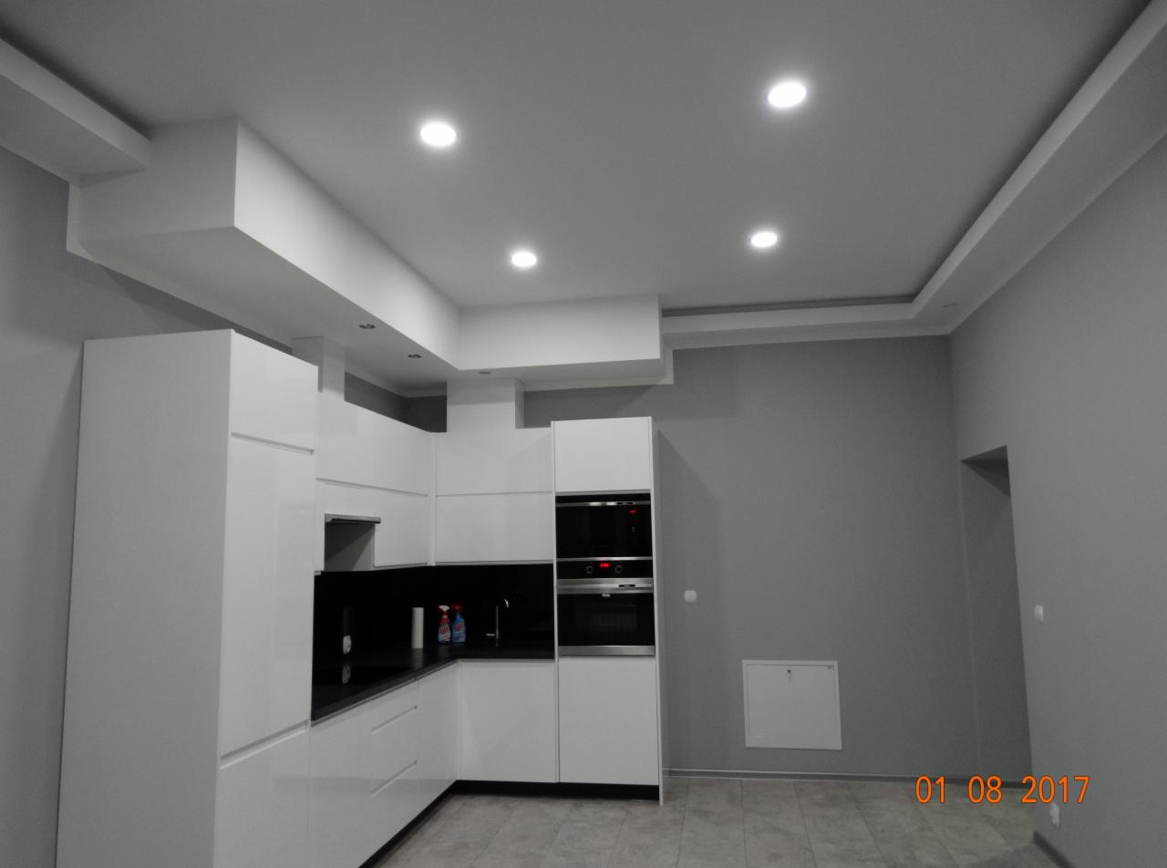 Nowoczesna, biała kuchnia z czarnymi blatami w Bielawie, szare ściany, oświetlenie sufitowe punktowe i dekoracyjny sufit podwieszany.