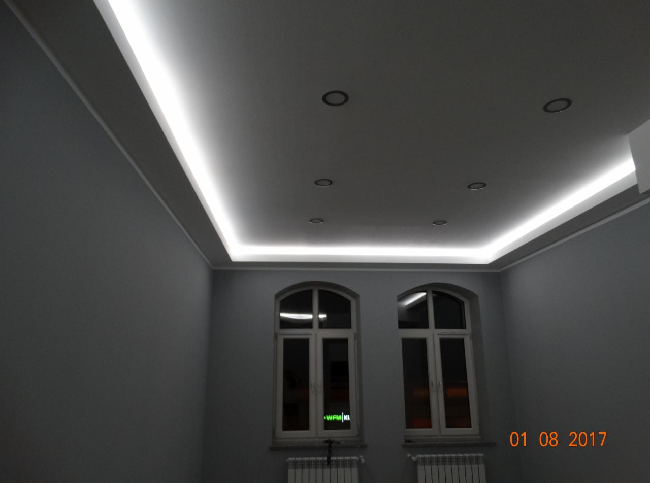 Pokój z szarymi ścianami, dwoma oknami z łukami, grzejnikami pod oknami i podwieszanym sufitem z oświetleniem LED na obwodzie oraz punktowymi lampami.