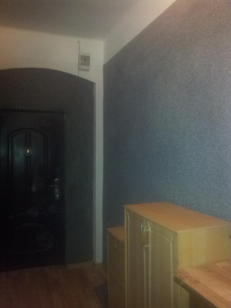 Ściana z szarą, ziarnistą fakturą w mieszkaniu w Zabrzu, obok ciemne drzwi z łukowatym nadprożem i drewniana szafka.