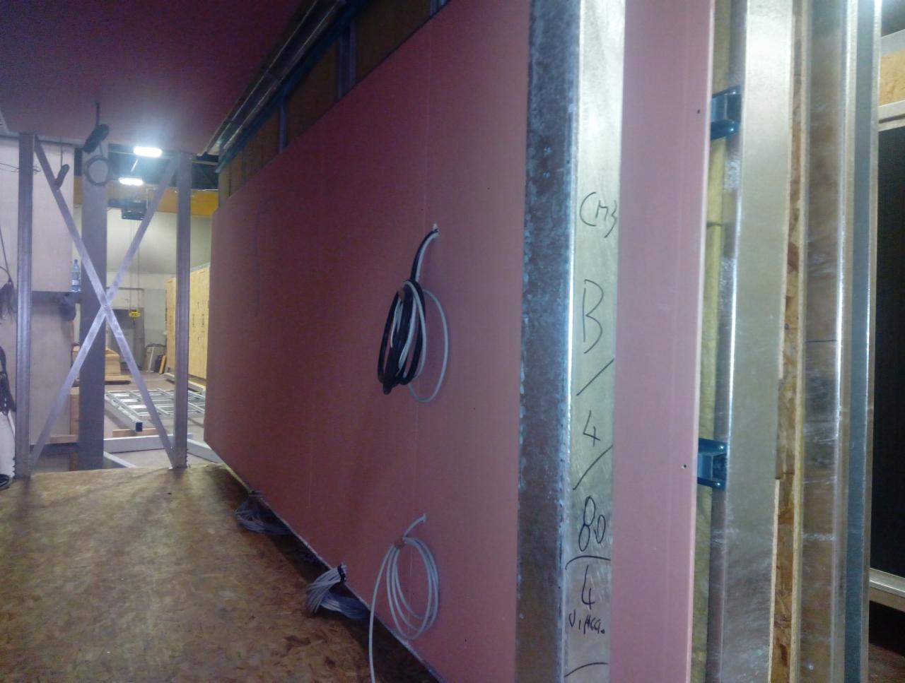 Montaż różowej płyty karton gips na metalowym stelażu, widoczne przewody elektryczne i notatki na profilu