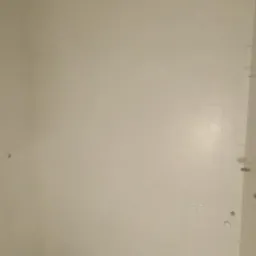 Świeżo wykafelkowana ściana łazienki z widocznymi fugami, jasnoszare płytki, fragment podłogi z pozostawionym otworem na odpływ.