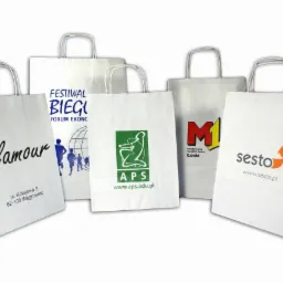 Białe papierowe torby z nadrukami reklamowymi różnych firm i wydarzeń, ustawione na białym tle, prezentujące różnorodność wzorów i kolorów.