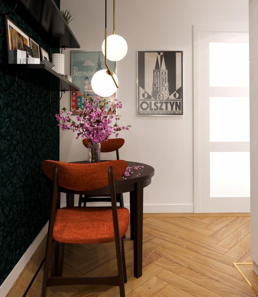 Jadalnia z okrągłym stołem, krzesłami w kolorze pomarańczowym, wiszącą lampą z kulistymi kloszami i plakatami z motywami miejskimi na ścianie, uzupełniona wazonem z kwitnącą wiśnią.