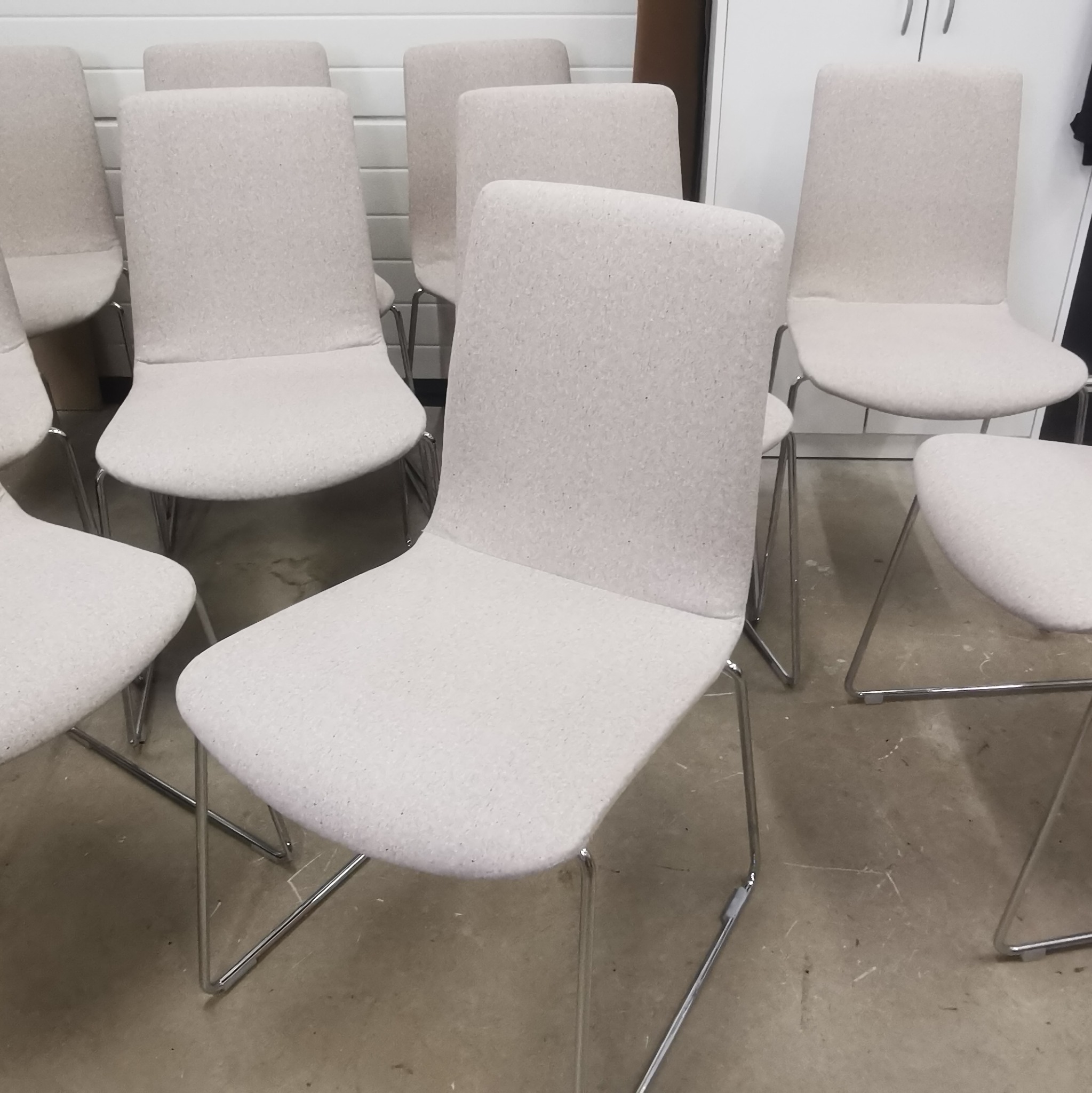 Rząd krzeseł z jasną tapicerką i metalowymi nogami, widoczne ślady użytkowania na podłodze.