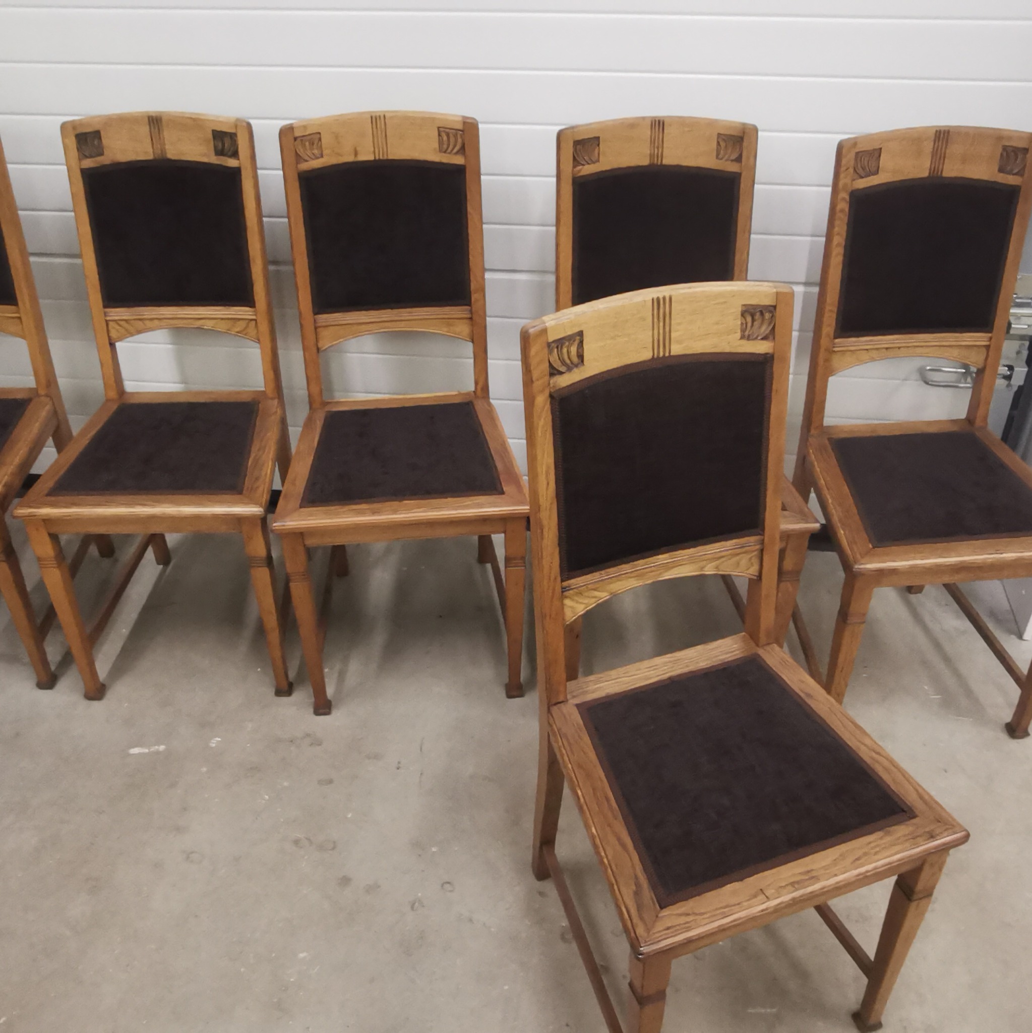 Rząd odnowionych krzeseł z drewnianymi ramami i ciemną tapicerką siedzisk i oparć, widoczne detale zdobień na oparciach.