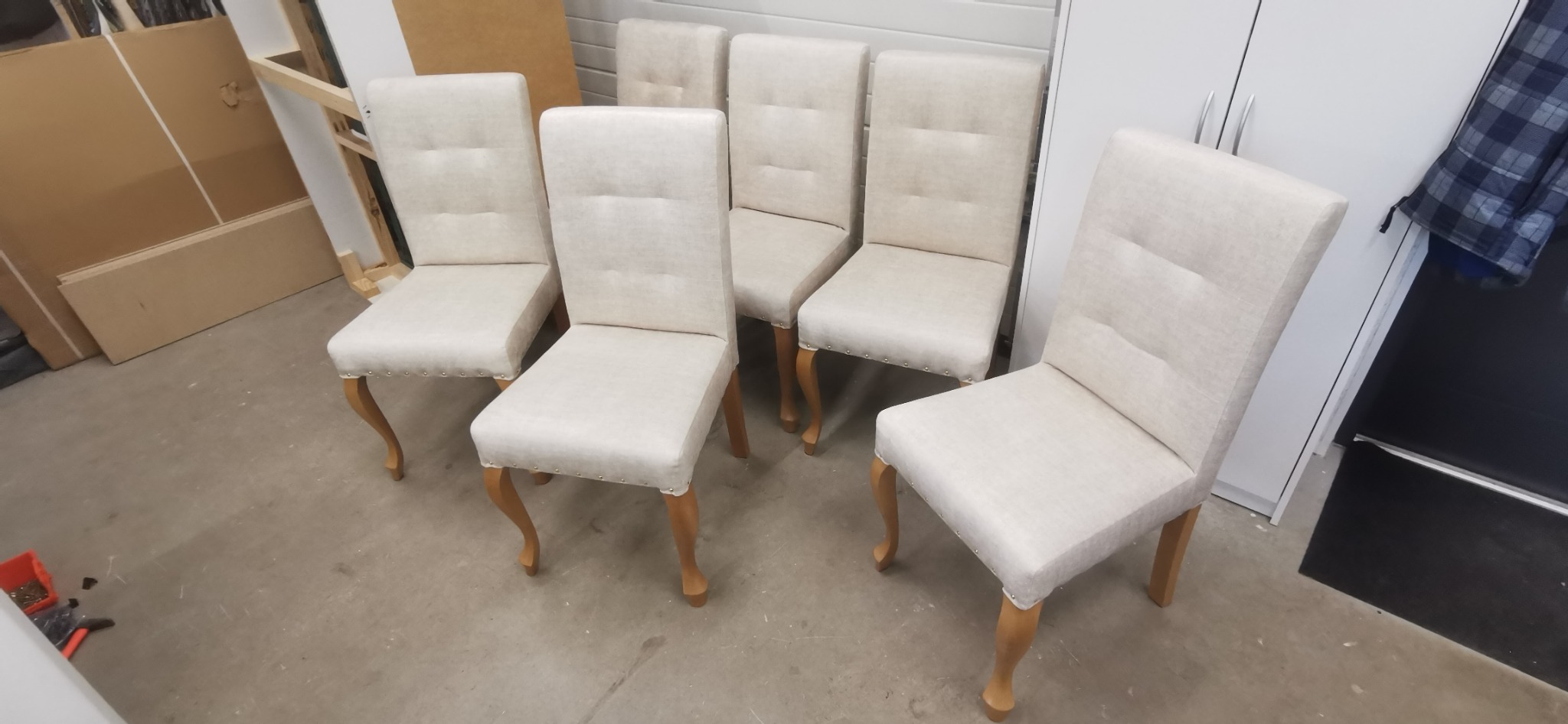 Sześć krzeseł po renowacji z jasną tapicerką i drewnianymi nogami w stylu ludwikowskim, widoczne na tle warsztatu.