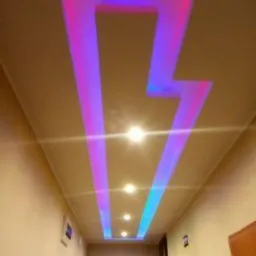Sufit z podświetlanym wzorem błyskawicy w odcieniach różu i błękitu, wzdłuż korytarza z oświetleniem punktowym.