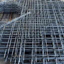 Siatka z prętów zbrojeniowych ułożona warstwami na betonowej posadzce, z widoczną etykietą z numerem partii na górze.