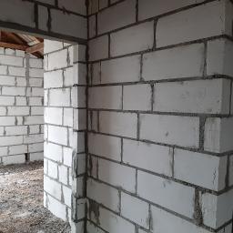 NOWY DOM Anna Serzysko - Wnętrze surowego domu w trakcie budowy, ściany wzniesione z białych bloczków, widoczne drewniane elementy konstrukcji dachu.