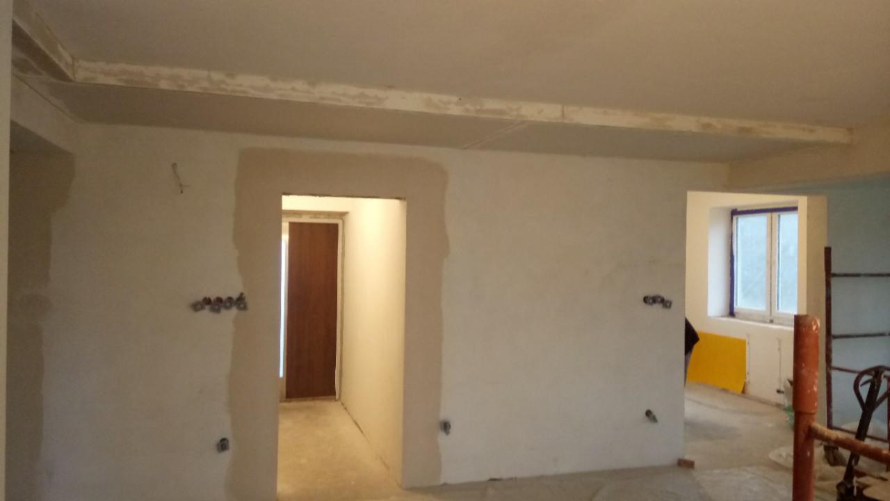 Wnętrze w trakcie prac wykończeniowych: ściany po gruntowaniu, widoczne puszki elektryczne, przygotowane ościeżnice drzwi i okien, sufit z elementami płyty karton-gips.