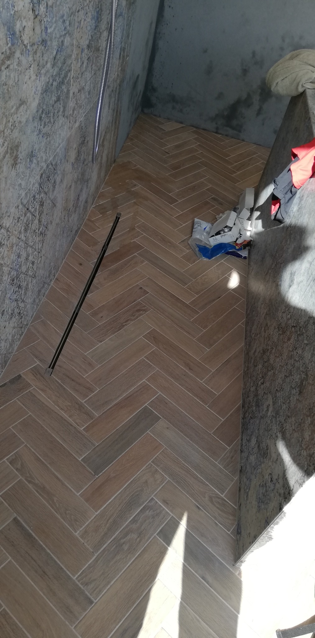 Ułożona w jodełkę podłoga z płytek imitujących drewno w kabinie prysznicowej we Wrocławiu, z widocznym odpływem liniowym i fragmentem ściany wyłożonej płytkami o wzorze przypominającym kamień.