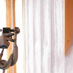 Pracownik w kombinezonie ochronnym aplikuje białą piankę PUR na drewniany szkielet budynku za pomocą pistoletu natryskowego.