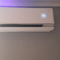 Biały klimatyzator Rotenso zamontowany na szarej ścianie, wyświetlający temperaturę 30 stopni Celsjusza, z widoczną listwą sufitową.