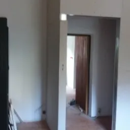 Remontowany pokój z widocznymi płytami karton gips na ścianach i suficie, surowy stan wykończenia, drewniana podłoga z widocznymi śladami po remoncie.