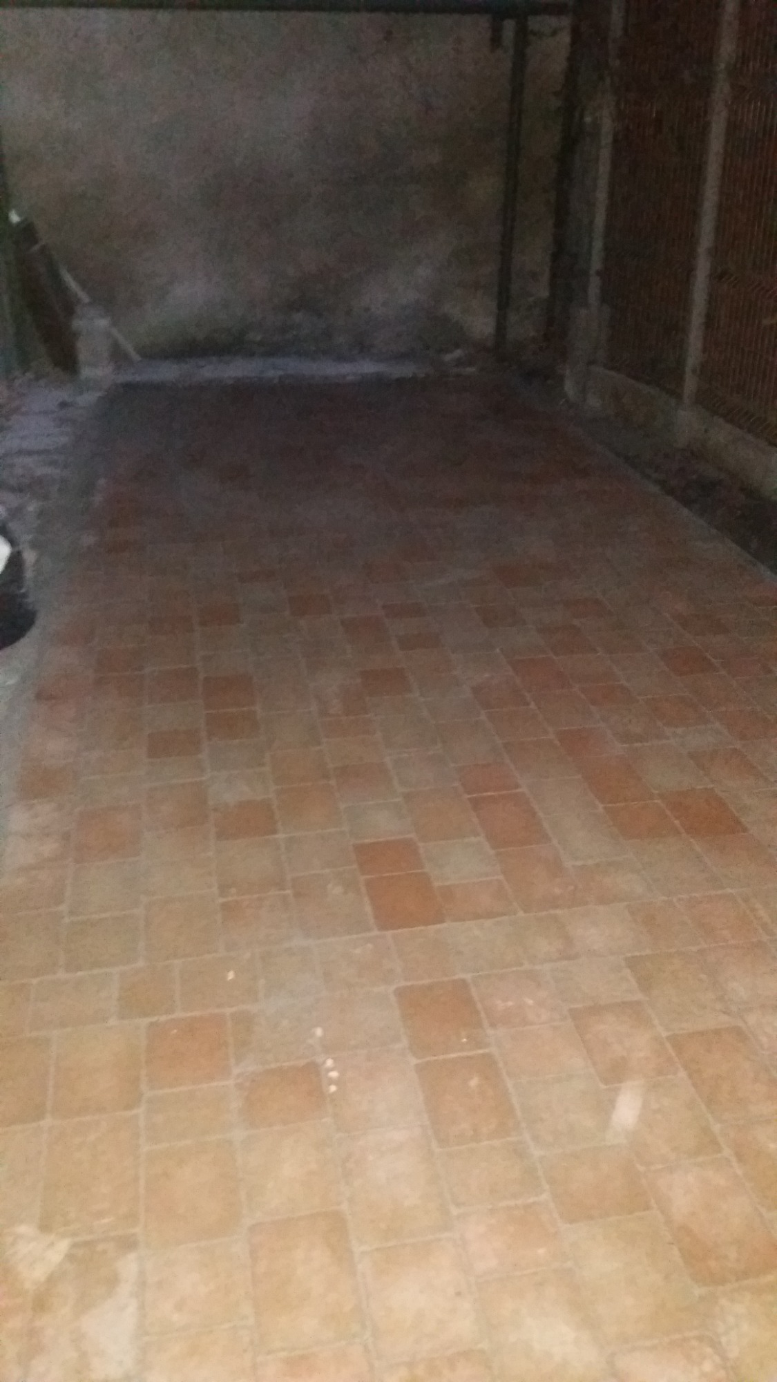 Ułożona terakota w ciemnym pomieszczeniu, widoczne ślady po zaprawie, surowe ściany w tle.