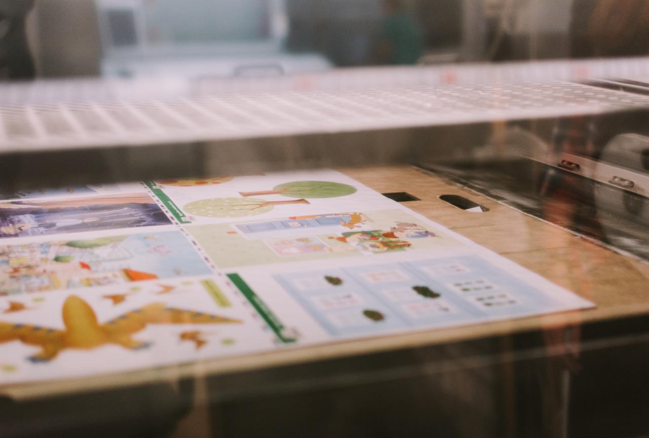 Arkusze z kolorowymi ilustracjami dla dzieci wewnątrz maszyny drukarskiej, oświetlenie studyjne.