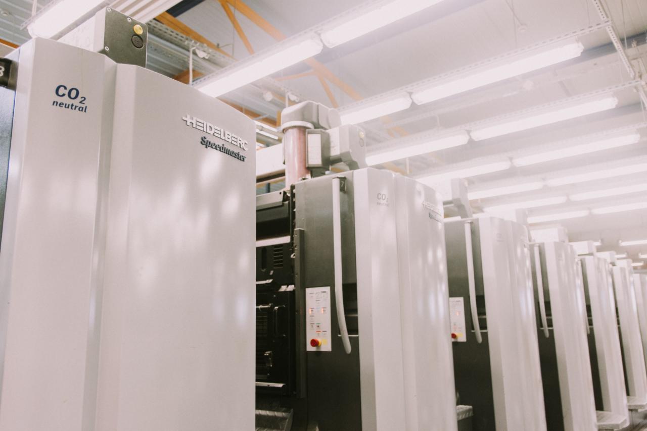 Rząd białych maszyn drukarskich Heidelberg Speedmaster w hali produkcyjnej, z widocznym napisem 'CO2 neutral' na jednej z nich.