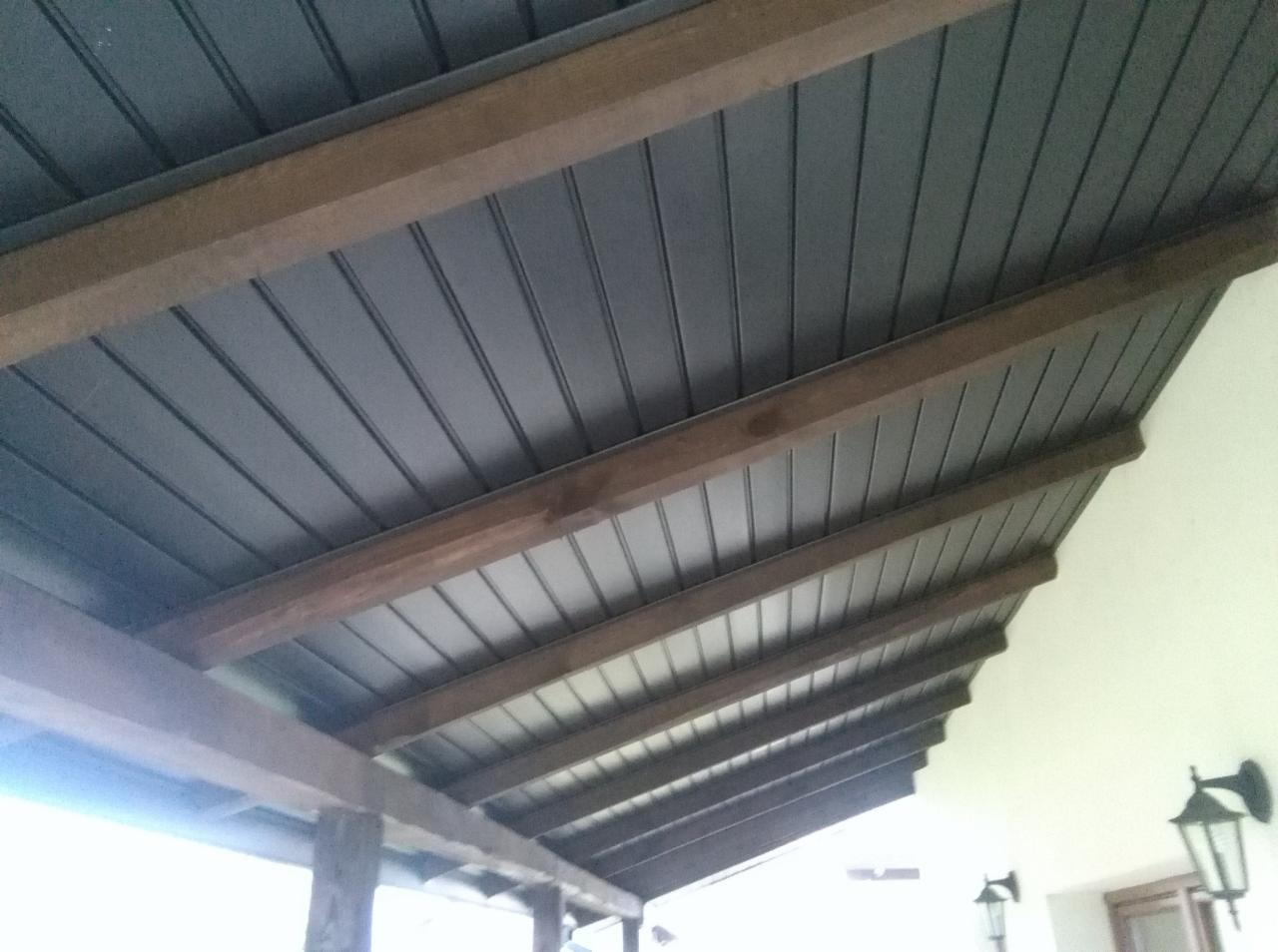 Podbitka dachu z ciemnoszarych paneli blaszanych, zamontowana na drewnianej konstrukcji z belek, widok z dołu na zewnątrz budynku.