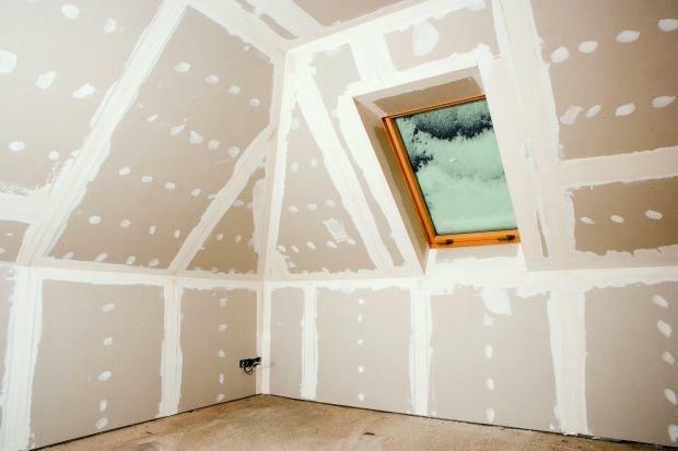 Poddasze w trakcie wykańczania płytami gipsowo-kartonowymi, widoczne łączenia wzmocnione taśmą i szpachlowane, okno dachowe w drewnianej ramie, surowy beton na podłodze.