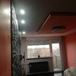 Pomarańczowe ściany i sufit w pokoju z czarną, kamienną ścianą akcentującą, grzejnikiem pod oknem i zamontowanym uchwytem ściennym na telewizor.