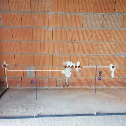 Wewnętrzne okablowanie elektryczne w surowym budynku z cegły, z widocznymi puszkami instalacyjnymi i przewodami, mierzone od podłogi.