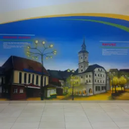 Ilustracja na ścianie przedstawiająca historyczny dworzec i ratusz w Gliwicach, z tekstem informacyjnym powyżej.