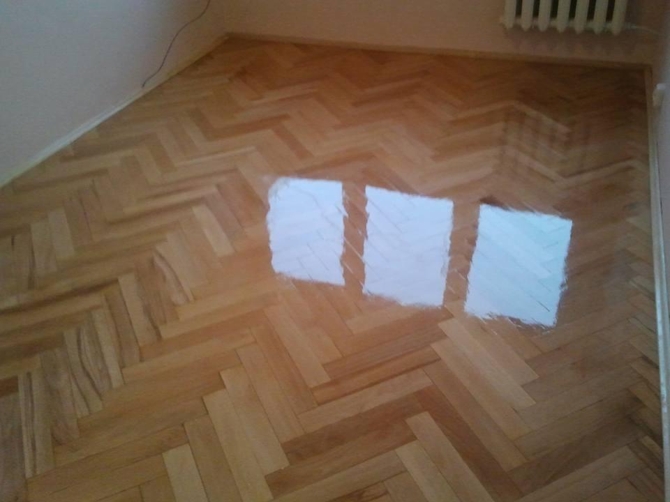 Parkiet ułożony w jodełkę, świeżo polakierowany, z widocznymi refleksami światła na powierzchni.