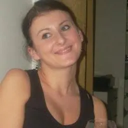 Portret kobiety w czarnej bluzce na neutralnym tle, z delikatnym uśmiechem i upiętymi włosami.