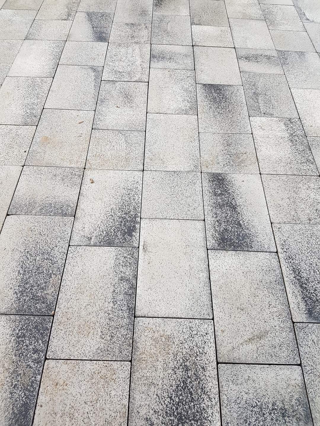 Ułożona szara kostka brukowa o nieregularnym wzorze i ciemniejszych akcentach, widziana z perspektywy ukośnej.