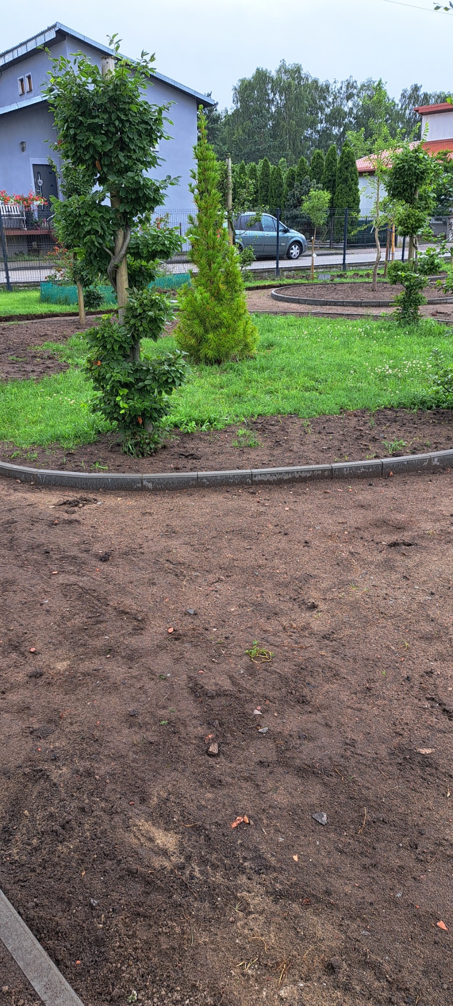 Przygotowany teren pod trawnik i nasadzenia w Kołczygłowach, obrzeża z kostki brukowej, widoczne ślady po pracach ziemnych.